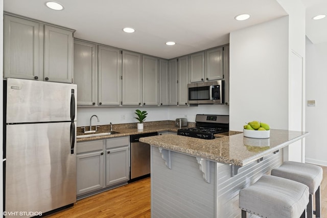 kitchen with appliances with stainless steel finishes, gray cabinets, a sink, recessed lighting, and light wood-style floors