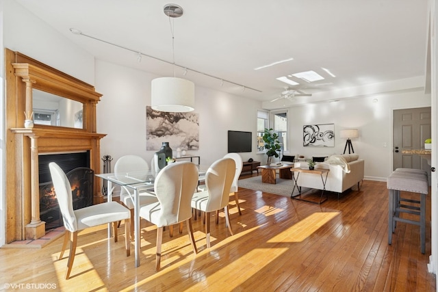 dining space featuring wood-type flooring, a lit fireplace, track lighting, and a ceiling fan