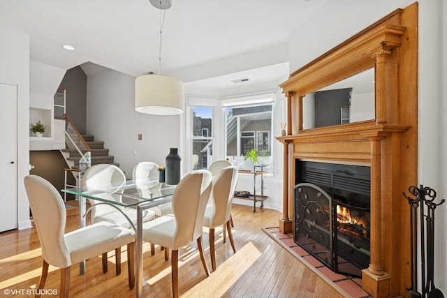 dining space with light wood-style floors, a lit fireplace, stairs, and recessed lighting