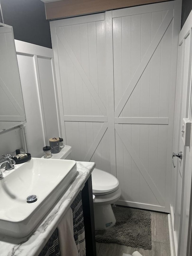 2493 W Mud Creek Rd, Mount Morris, IL 61054 - half bathroom featuring a decorative wall, toilet, vanity, and wood finished floors
