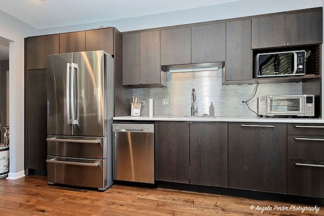kitchen with appliances with stainless steel finishes, a sink, light countertops, light wood-style floors, and dark brown cabinetry