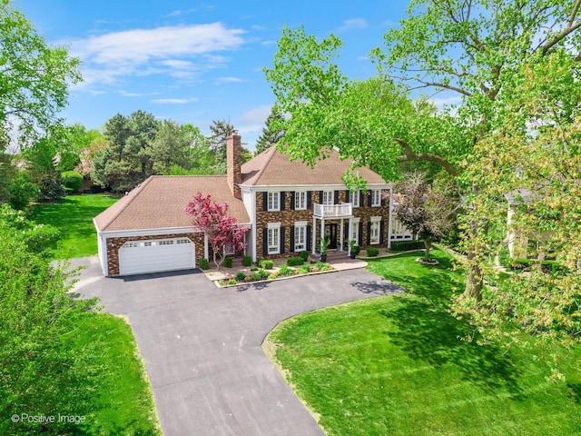 colonial-style house featuring a balcony, a front lawn, asphalt driveway, a chimney, and a garage