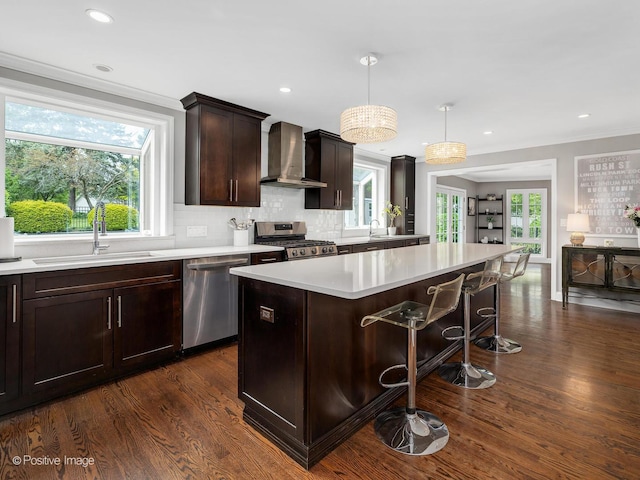 kitchen featuring wall chimney exhaust hood, appliances with stainless steel finishes, a sink, light countertops, and dark wood-type flooring