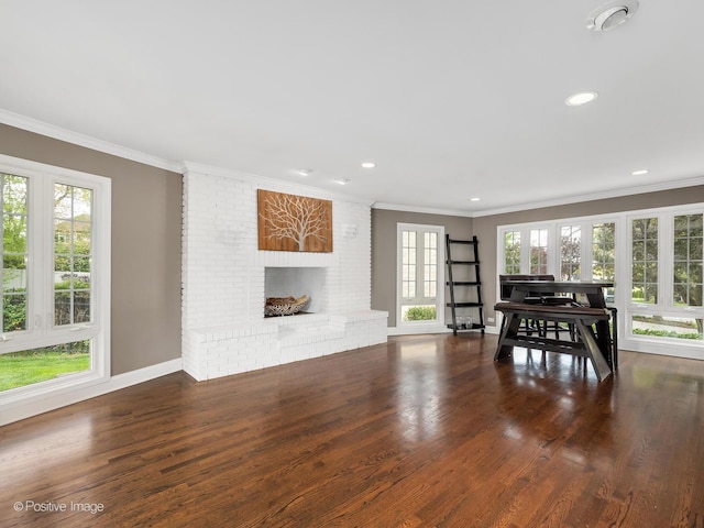living area featuring plenty of natural light, ornamental molding, wood finished floors, recessed lighting, and a brick fireplace