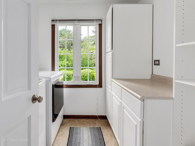 clothes washing area with separate washer and dryer, cabinet space, baseboards, and light tile patterned floors