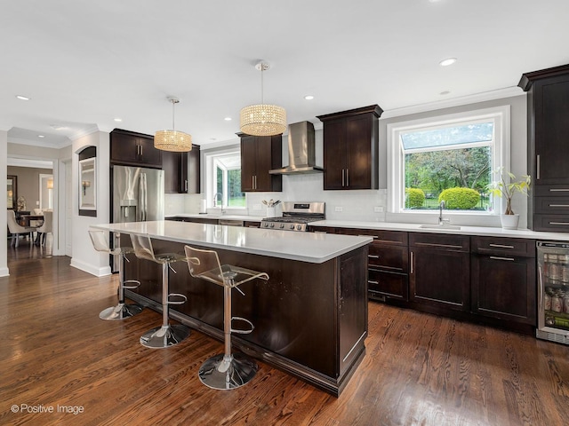 kitchen featuring wall chimney exhaust hood, stainless steel range, beverage cooler, a center island, and a sink