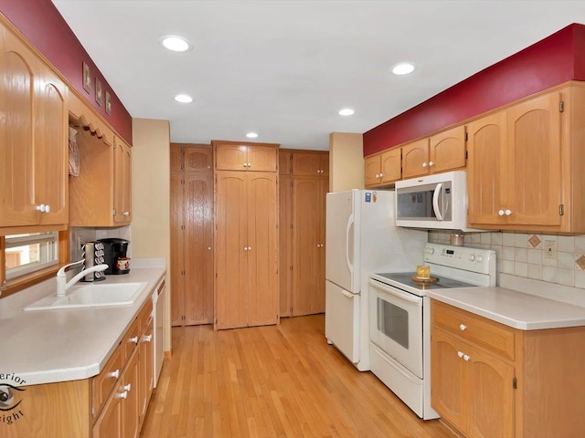 kitchen with white appliances, a sink, light countertops, light wood-type flooring, and recessed lighting