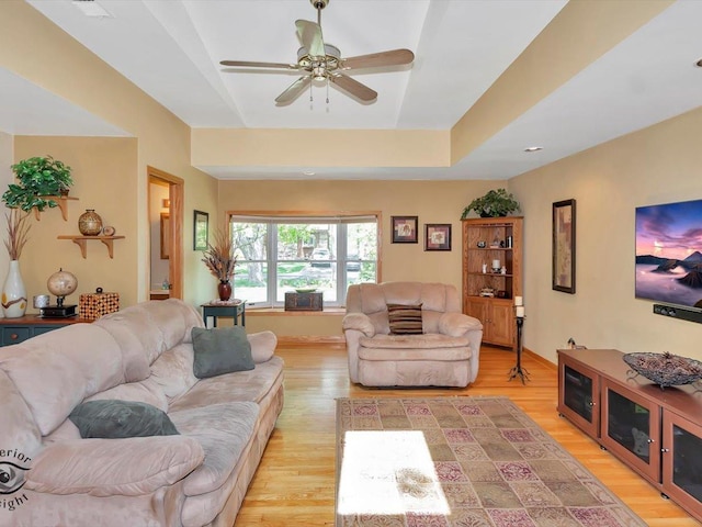 living room featuring light wood-style flooring, a raised ceiling, and a ceiling fan