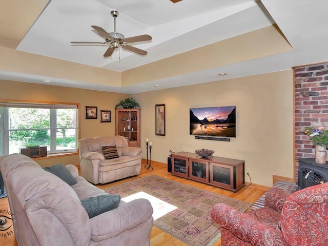 living area featuring a raised ceiling, a wood stove, light wood-style floors, and ceiling fan