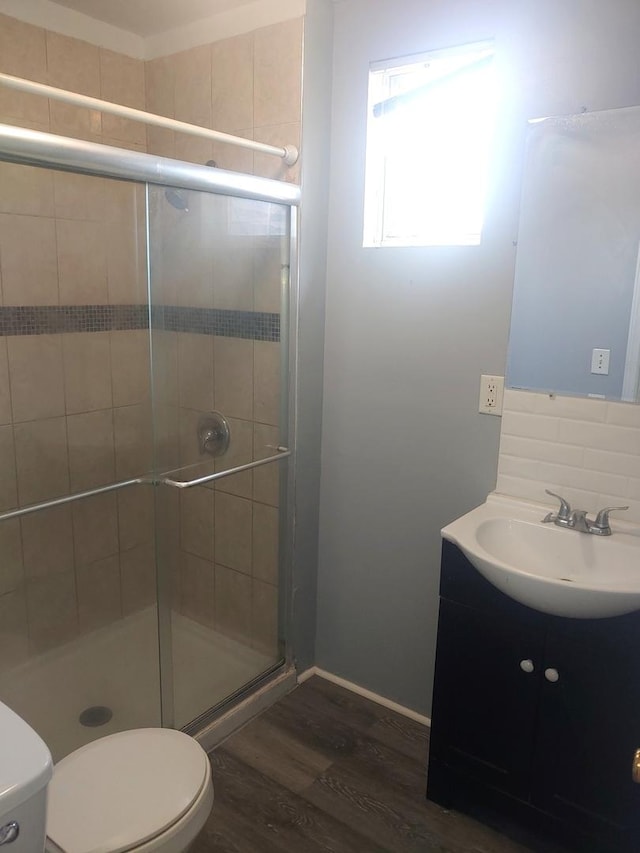 bathroom featuring toilet, wood finished floors, a shower stall, vanity, and backsplash
