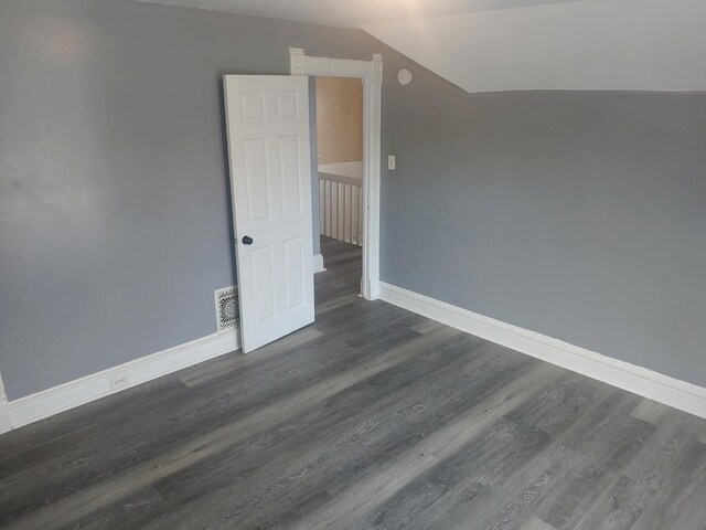 empty room with baseboards, lofted ceiling, and dark wood-style flooring