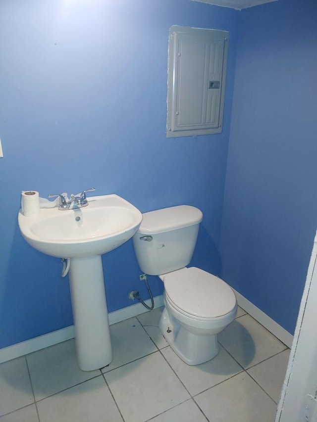 bathroom featuring electric panel, baseboards, toilet, tile patterned flooring, and a sink