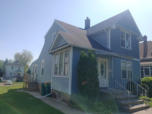 view of side of home with a chimney, a shingled roof, and a lawn