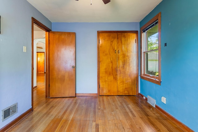 unfurnished bedroom with hardwood / wood-style flooring, arched walkways, baseboards, and a ceiling fan