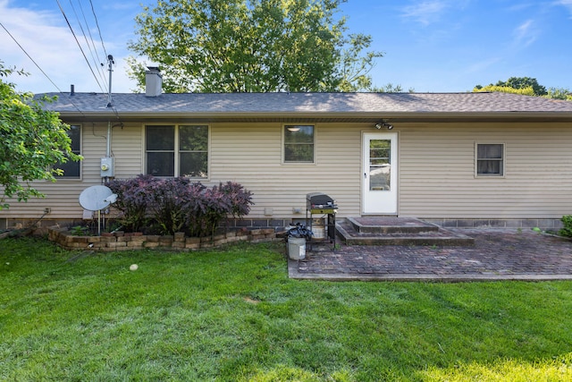 rear view of property with a lawn, a patio area, a chimney, and a shingled roof