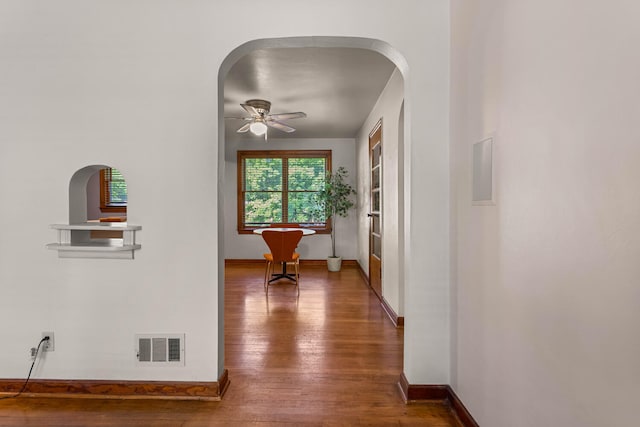 corridor with hardwood / wood-style floors, arched walkways, and baseboards