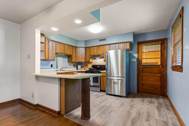 kitchen with stainless steel appliances, under cabinet range hood, brown cabinets, light wood-style flooring, and light countertops