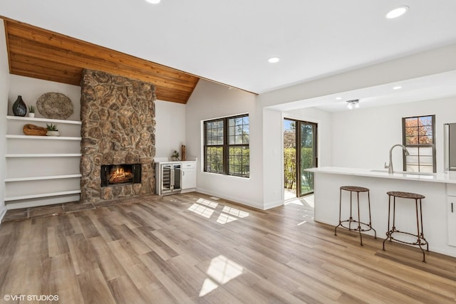 unfurnished living room featuring light wood-style floors, a sink, wine cooler, recessed lighting, and lofted ceiling