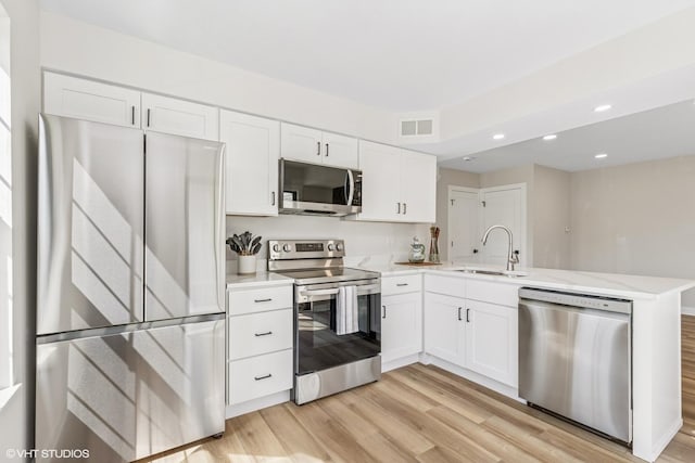 kitchen featuring stainless steel appliances, a sink, light wood-type flooring, a peninsula, and recessed lighting