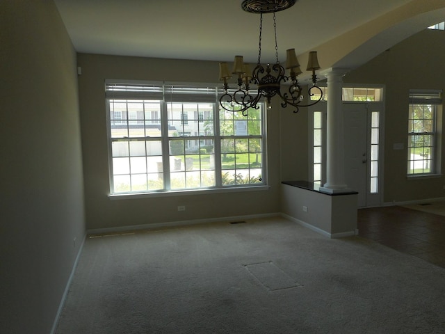 unfurnished dining area with baseboards, decorative columns, carpet, a chandelier, and arched walkways