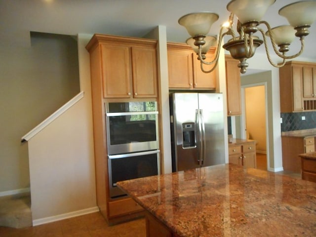 kitchen with stainless steel appliances, tasteful backsplash, dark stone counters, a chandelier, and baseboards