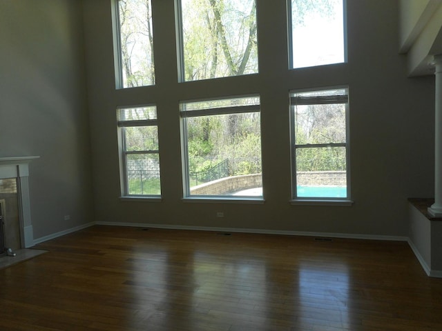 unfurnished living room with plenty of natural light, wood finished floors, baseboards, and a towering ceiling