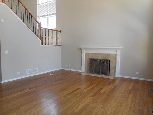 unfurnished living room with wood-type flooring, a tile fireplace, stairs, baseboards, and a towering ceiling