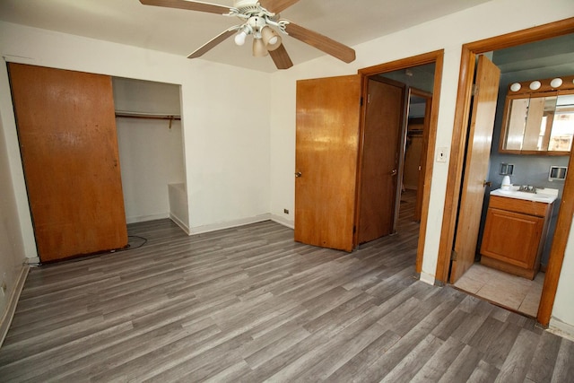 unfurnished bedroom with wood finished floors, a closet, a ceiling fan, baseboards, and a sink