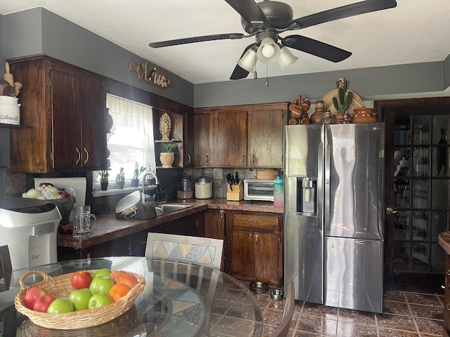 kitchen with stainless steel refrigerator with ice dispenser, a sink, ceiling fan, dark countertops, and decorative backsplash