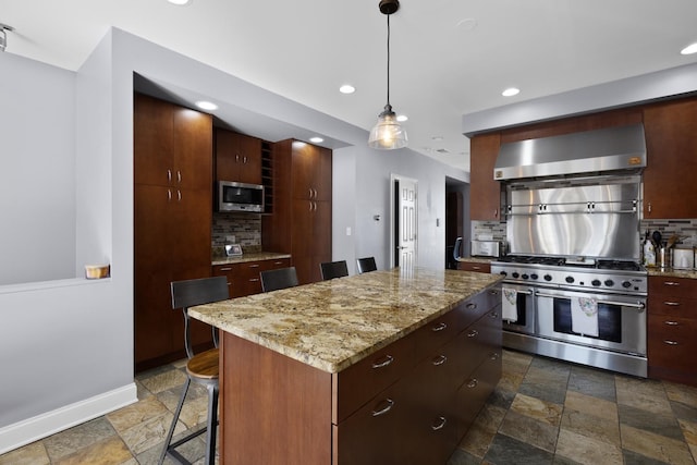 kitchen featuring stainless steel appliances, wall chimney exhaust hood, stone tile flooring, decorative backsplash, and a center island