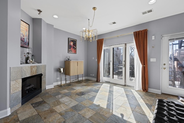 unfurnished living room featuring stone tile floors, baseboards, a chandelier, a tiled fireplace, and recessed lighting