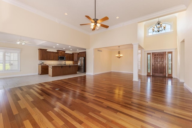 unfurnished living room featuring a chandelier, a high ceiling, light wood-style floors, ceiling fan, and crown molding