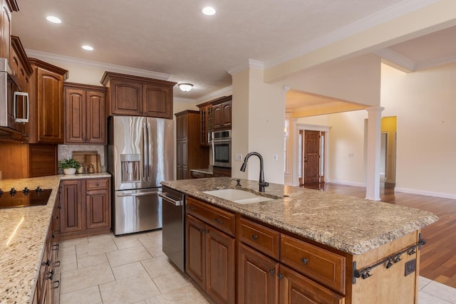 kitchen featuring appliances with stainless steel finishes, a sink, crown molding, a center island with sink, and decorative backsplash