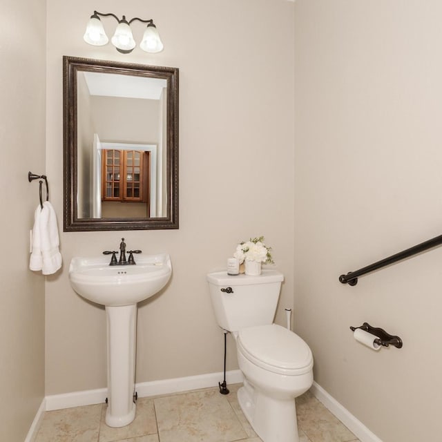 half bath featuring toilet, baseboards, tile patterned floors, and a sink