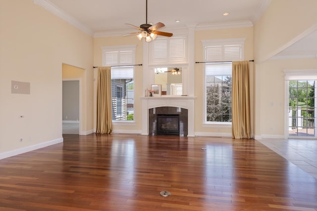 unfurnished living room with a towering ceiling, ceiling fan, crown molding, a glass covered fireplace, and wood finished floors