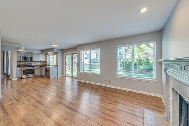 unfurnished living room with a fireplace with flush hearth, baseboards, a sink, light wood finished floors, and recessed lighting