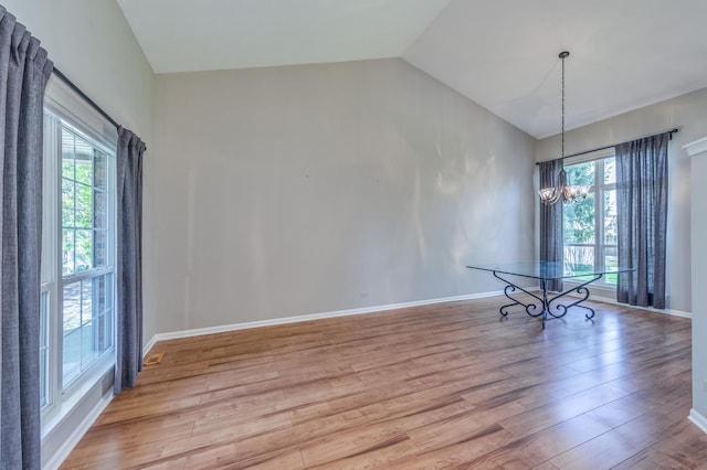 spare room featuring a chandelier, light wood-style flooring, vaulted ceiling, and baseboards