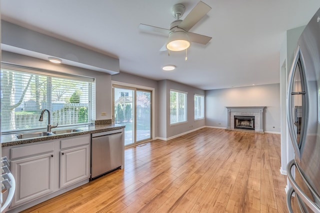 kitchen featuring appliances with stainless steel finishes, a sink, open floor plan, white cabinets, and light wood-type flooring