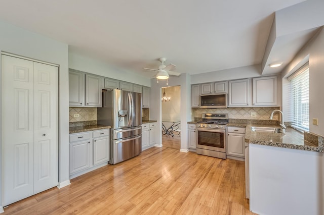 kitchen featuring stainless steel appliances, a sink, decorative backsplash, light wood finished floors, and ceiling fan