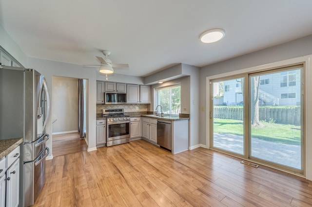 kitchen featuring stainless steel appliances, a sink, backsplash, and light wood-style flooring