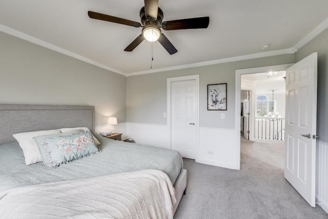carpeted bedroom with ornamental molding, a chandelier, a wainscoted wall, and ceiling fan