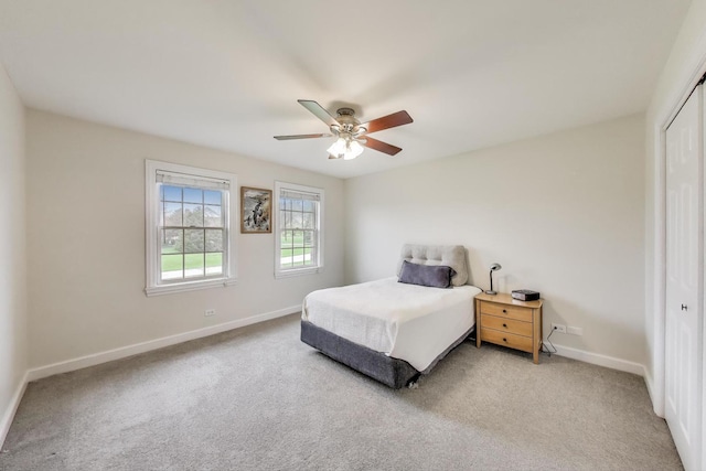 bedroom featuring a closet, light carpet, baseboards, and a ceiling fan