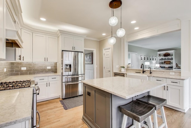 kitchen featuring appliances with stainless steel finishes, a kitchen island, light wood-style flooring, light stone countertops, and crown molding