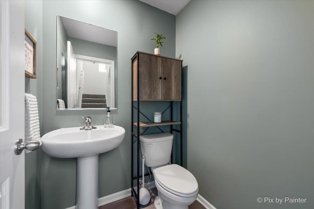 half bath featuring toilet, baseboards, and a sink