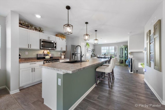 kitchen featuring appliances with stainless steel finishes, a sink, white cabinetry, an island with sink, and backsplash