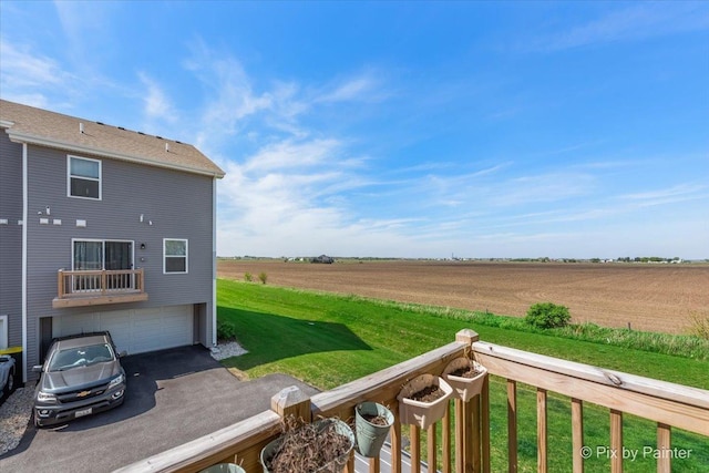 view of grassy yard featuring driveway, a view of countryside, a garage, and agricultural plots