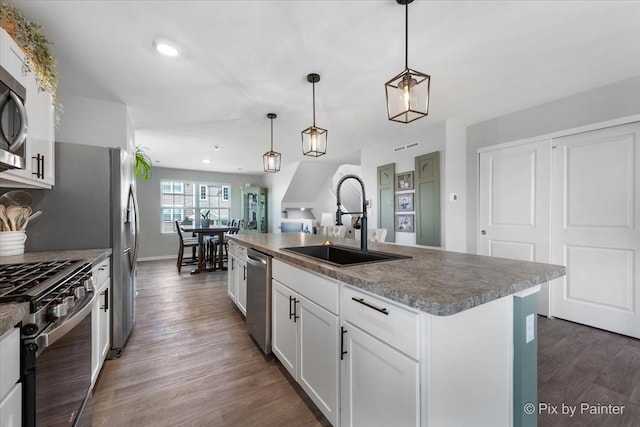 kitchen with a sink, stainless steel appliances, wood finished floors, white cabinetry, and hanging light fixtures