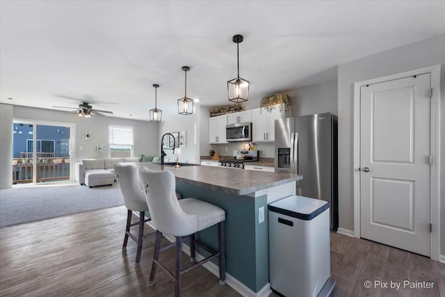 kitchen featuring appliances with stainless steel finishes, a sink, a breakfast bar area, white cabinets, and dark wood-style floors