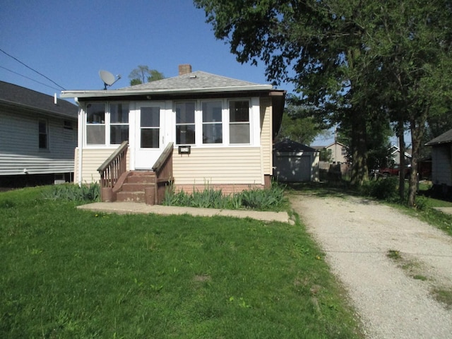 view of front of home with entry steps, driveway, a front yard, and a chimney