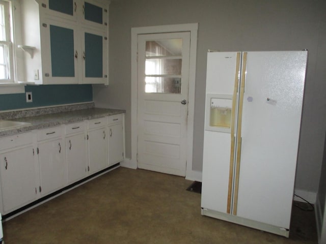 kitchen featuring white refrigerator with ice dispenser, white cabinets, light countertops, a sink, and dark colored carpet